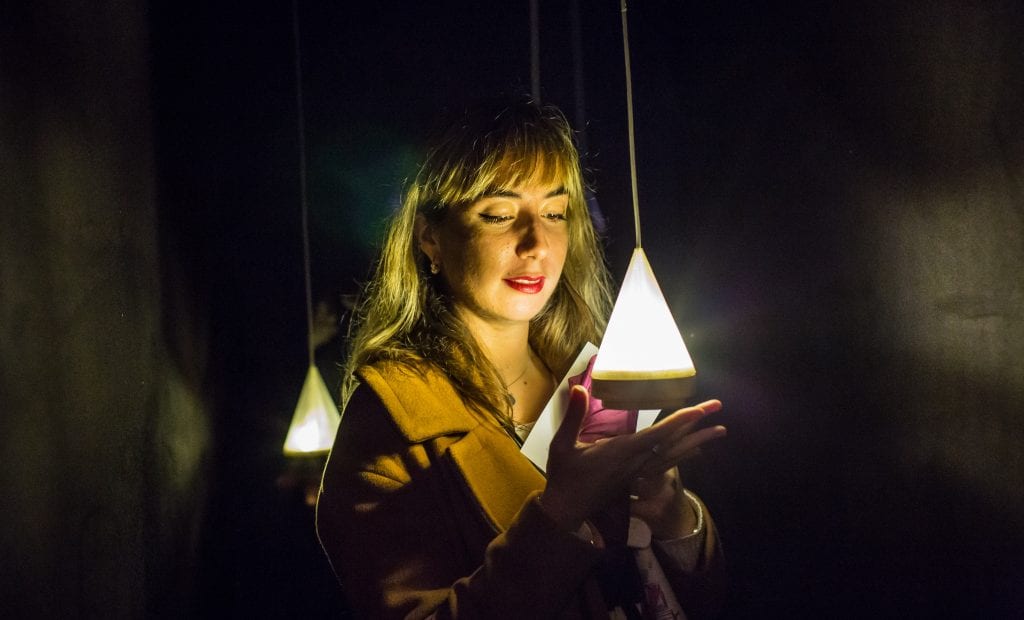 Woman holds hand underneath triangular light bulb dangling from ceiling.