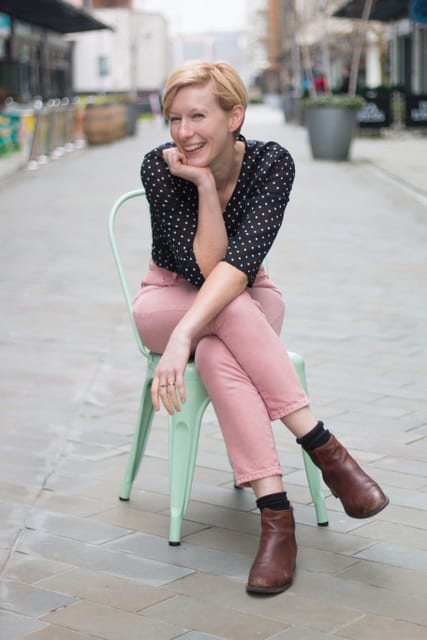 Jo Lansdowne sits on green chair smiling at camera.