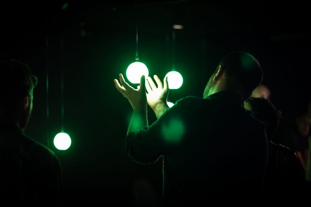 Man cups hands around green lightbulb at Squidsoup AudioWAVE.