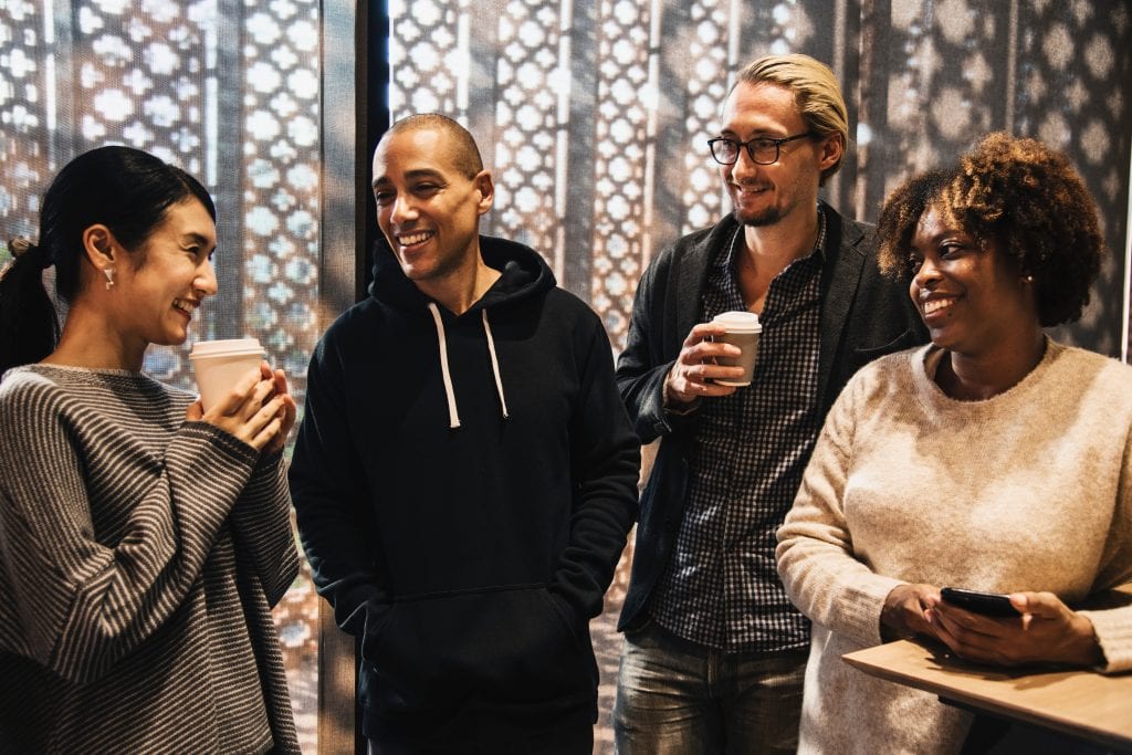 4 people stand smiling at one another.