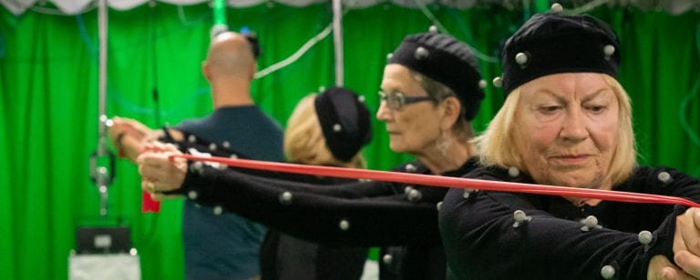 Two women in black suits and hats with dots stretching a red piece of elastic between them.