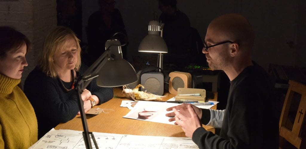 Man sits across table from two women looking at hand-drawn diagrams.