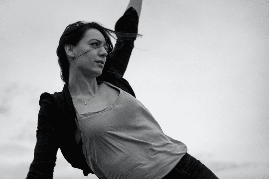 Black and white image of Adrienne Hart with hair blowing in wind and one arm reaching upwards.