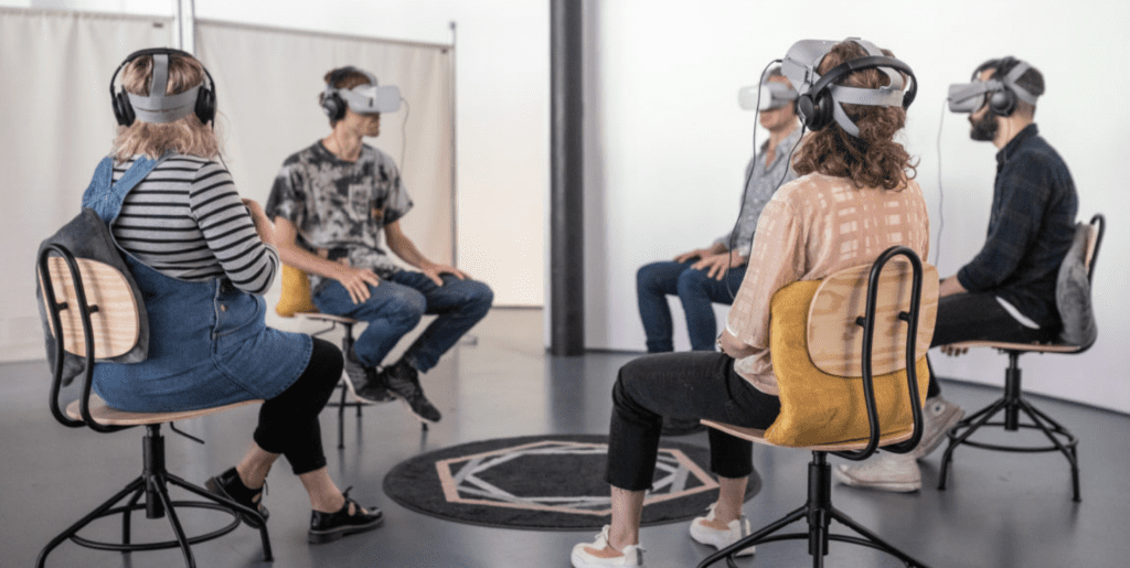 Group of 5 people sat on chairs in a circle wearing VR headsets.