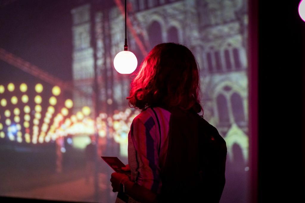 Person looks at pink glowing lightbulb in art installation.