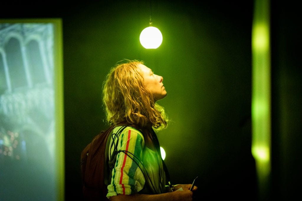 Person stands under green lightbulb in light installation.