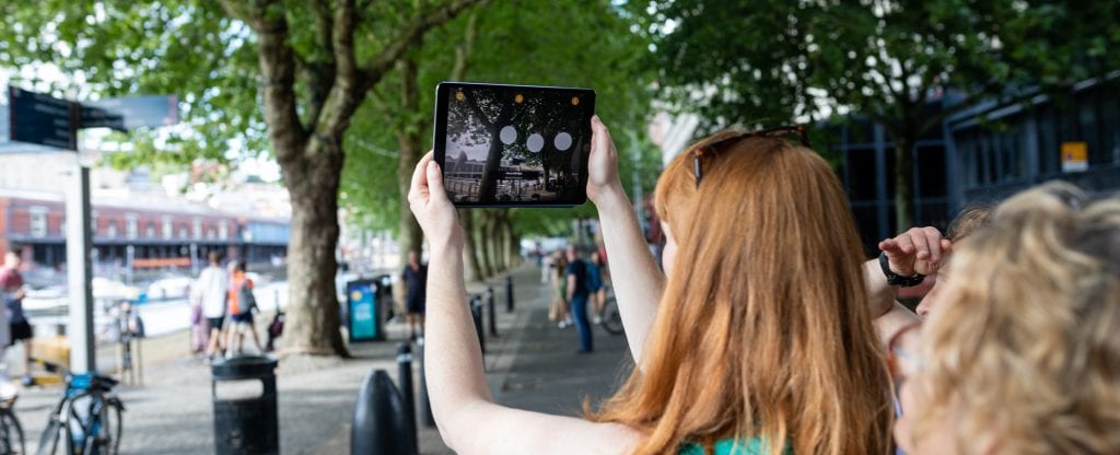 Woman holds tablet up to trees and screen shows information circles around image.