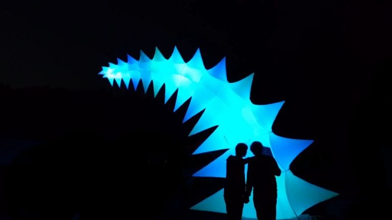 Two people stand in front of large spiky blue model.