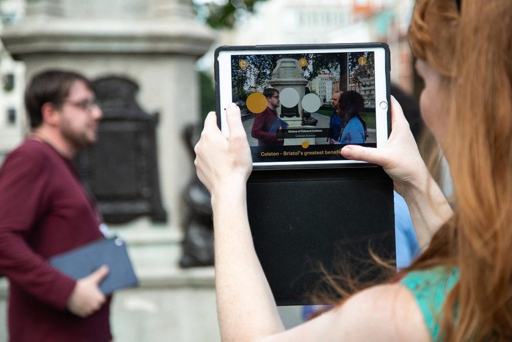 Woman holds tablet up to statue in front of her and it shows information about it.