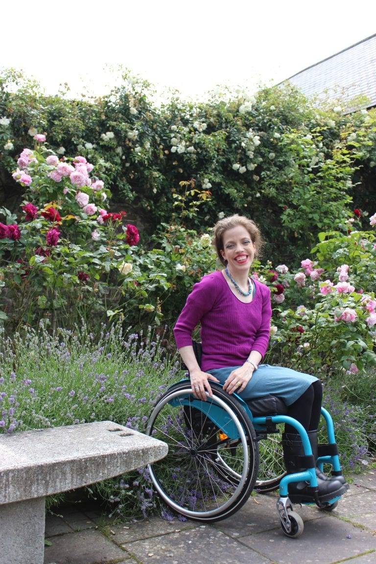 Grace Quantock sitting in front of a lavender bush, smiling in a wheelchair.