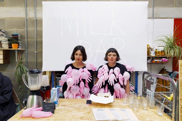 Conway and Young wearing t-shirts with handshaped balloons attached, with the words 'Milk Bar' in the background.