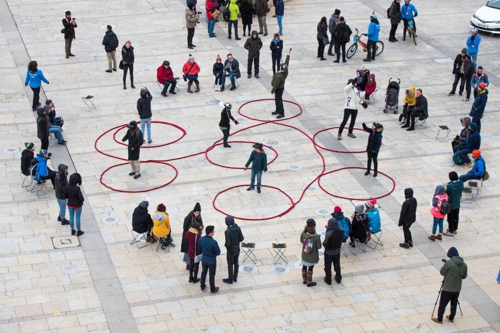 Long piece of rope made into loops with a person standing in each loop while a crowd watches.