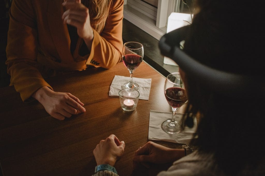 2 people sit across from each other at table with a glass of red wine each.