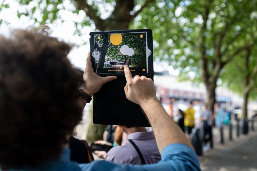 Someone using tablet pointed towards trees, screen shows lights in front of trees.