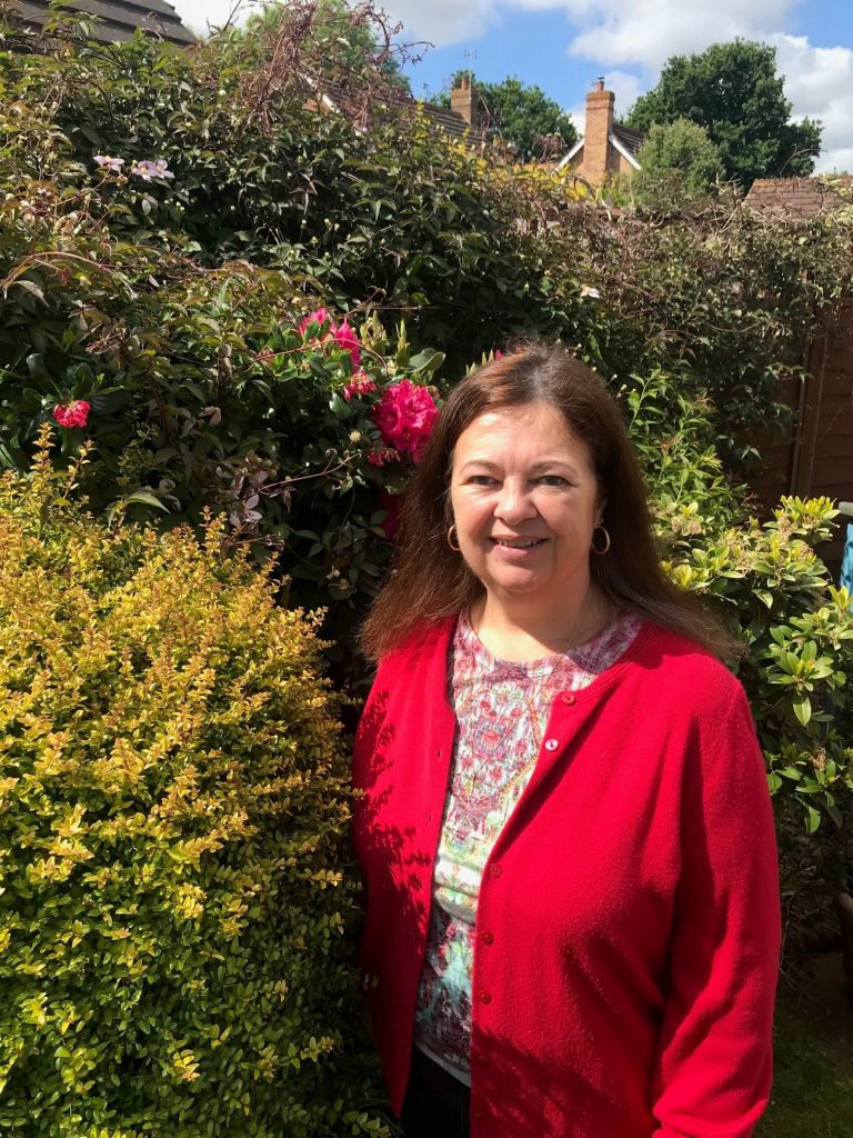 Gizelle Allan outdoors, smiling at camera, next to rose bush.