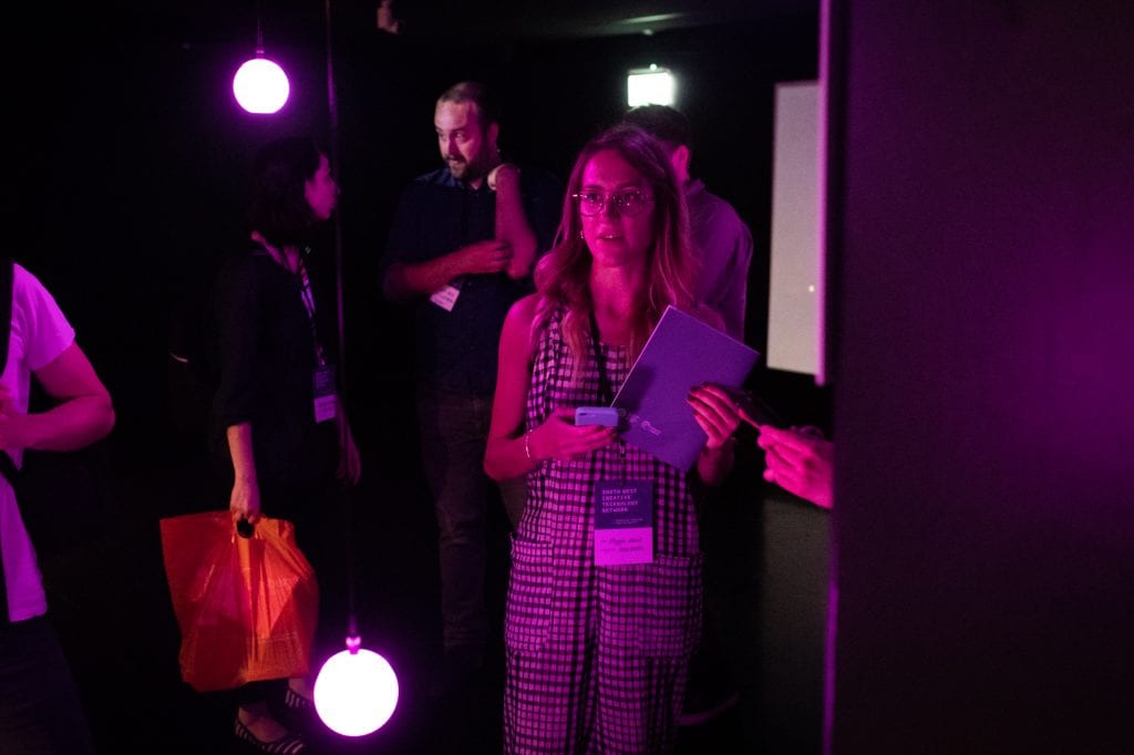 Woman holding notebook and phone stands in purple-lit room at light installation