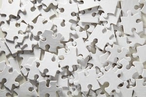 A jumbled pile of jigsaw puzzle pieces. All the pieces are blank and white making the puzzle almost impossible to complete.