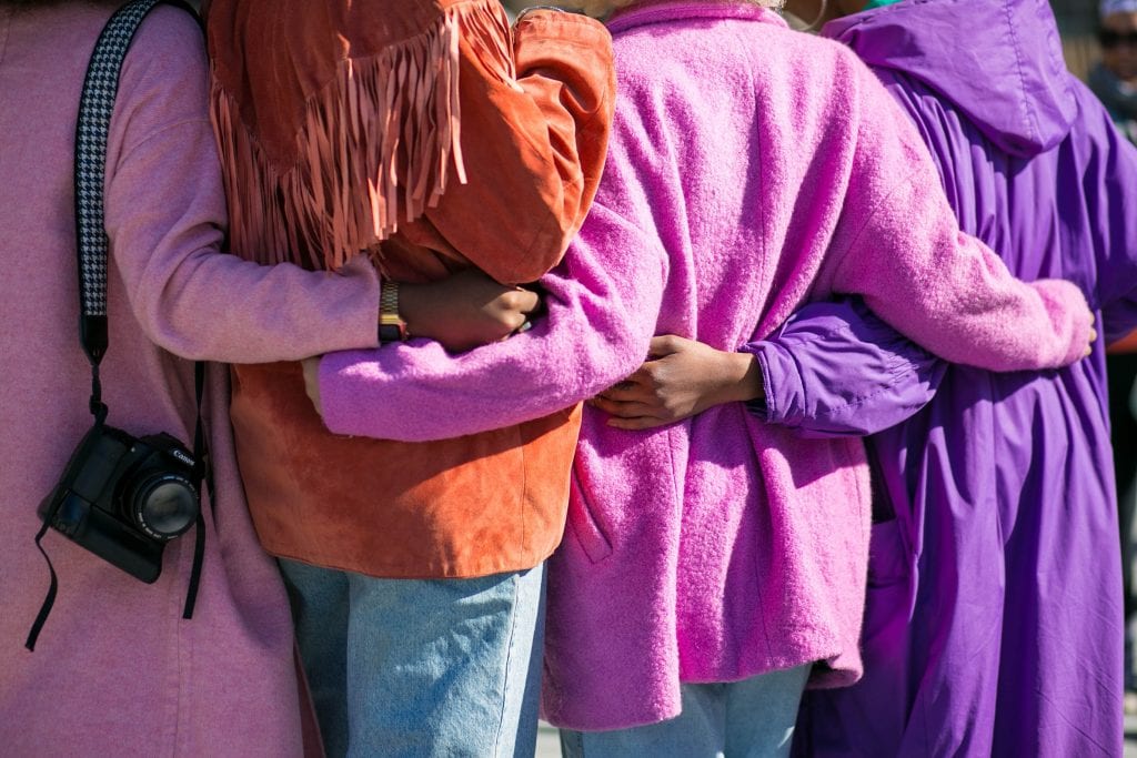 4 people standing with their arms around one another in colourful coats