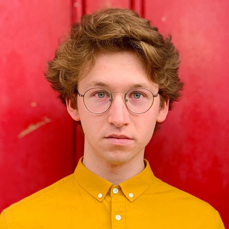 Alex Robins, New Creative. Alex wear a yellow shirt against a red background